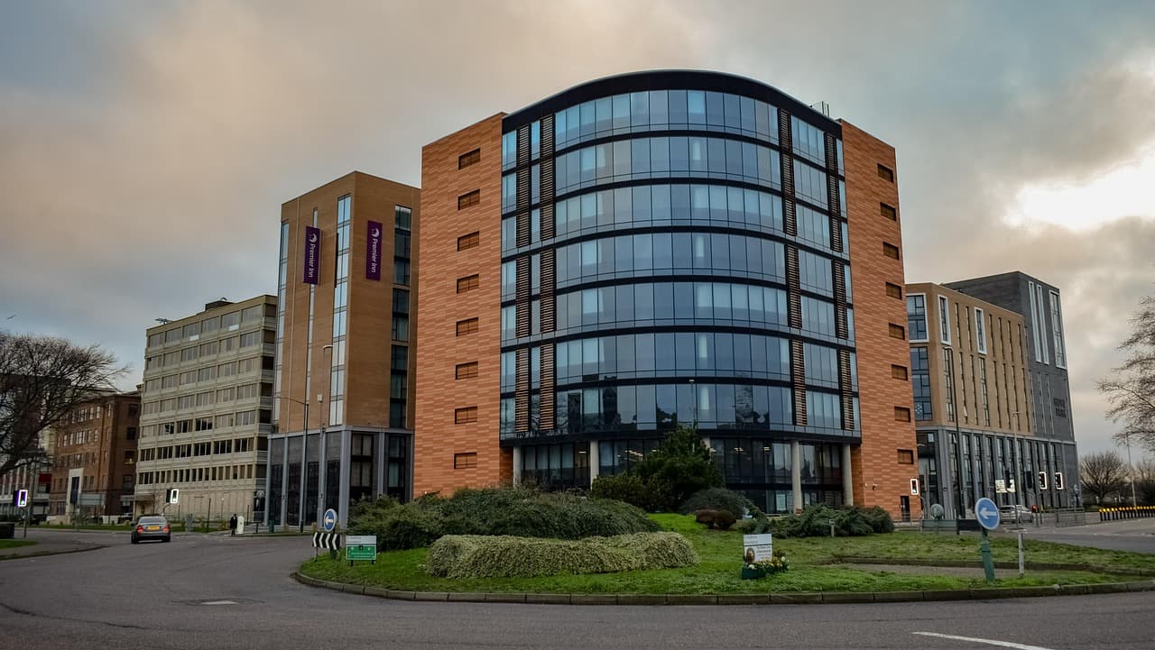A planted roundabout in front of new brick and glass buildings on an English ring road